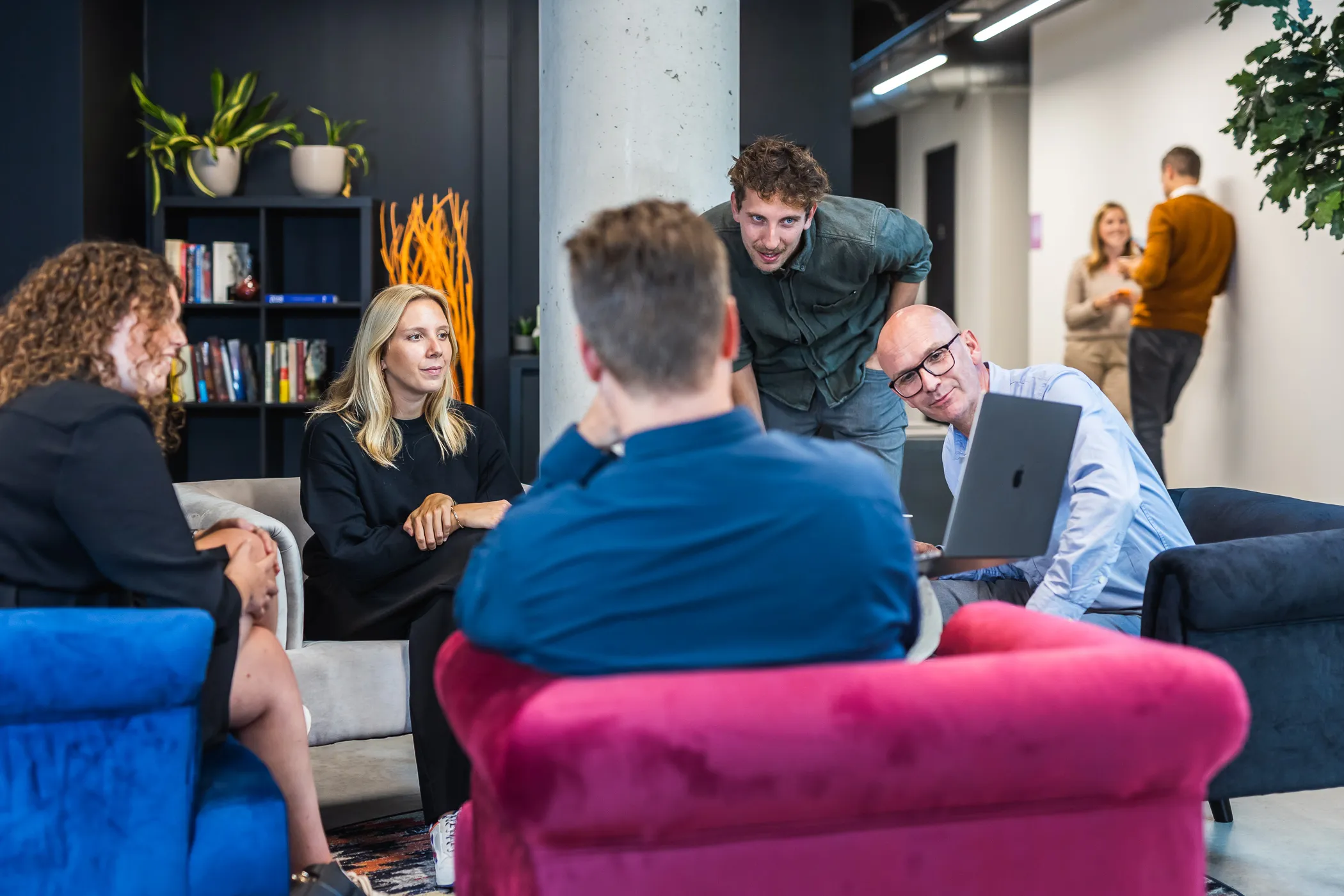 Collega's overleggen samen rond een laptop in de lounge van het Hasseltse kantoor.